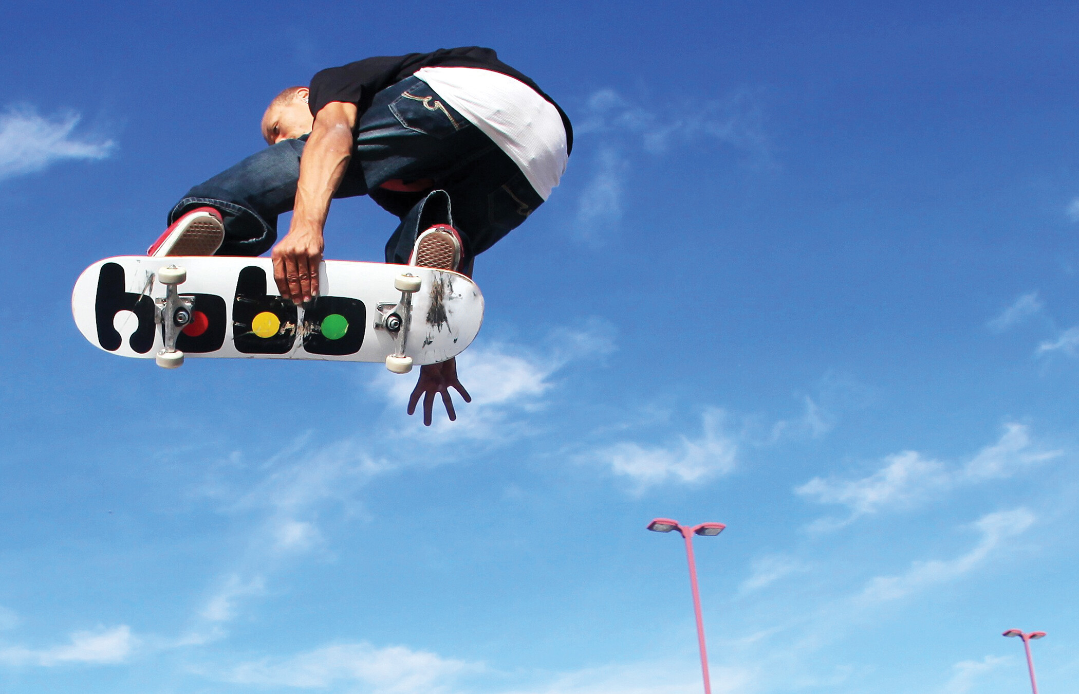 A skate boarder soars over the camera against a blue sky riding a Hobo Skate Company brinded board.