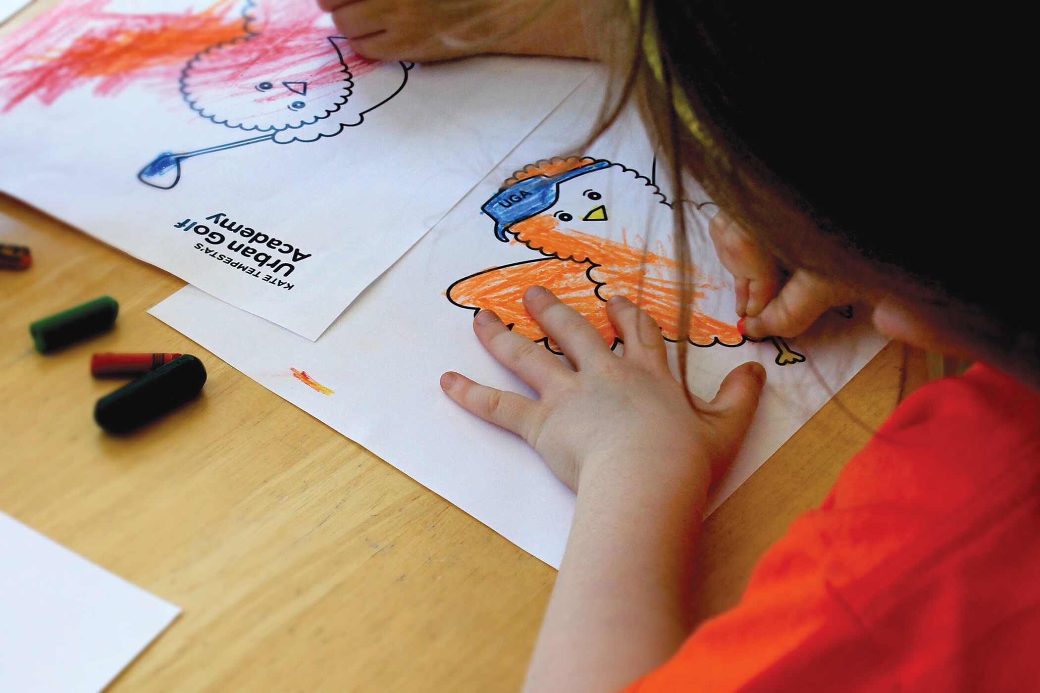 Close up of a student filling in a coloring book page of Birdie, the illustrated orange Urban Golf Academy mascot.